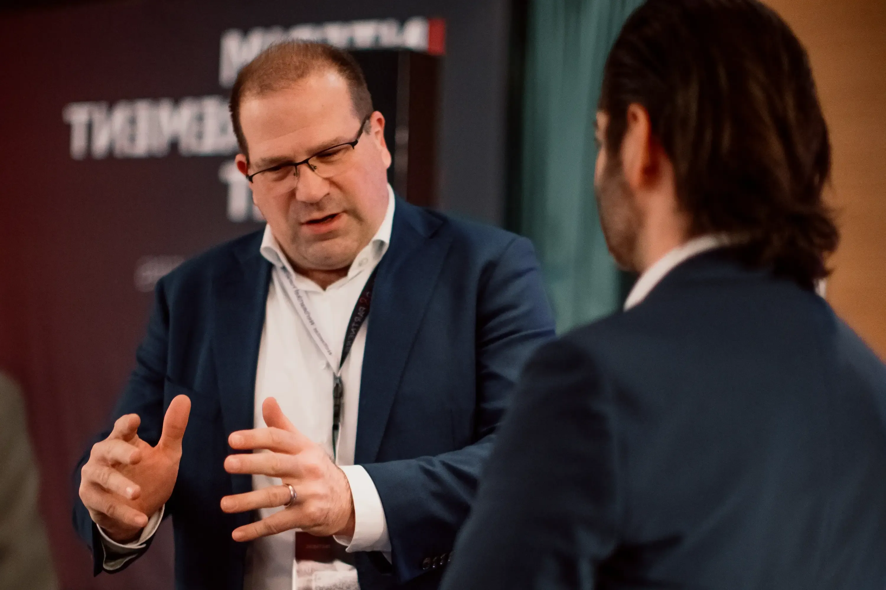 Tim spricht mit einem CEO Foto von Tim und zwei weiteren Männern, wie sie auf einer Konferenz miteinander Tim spricht mit einem CEO